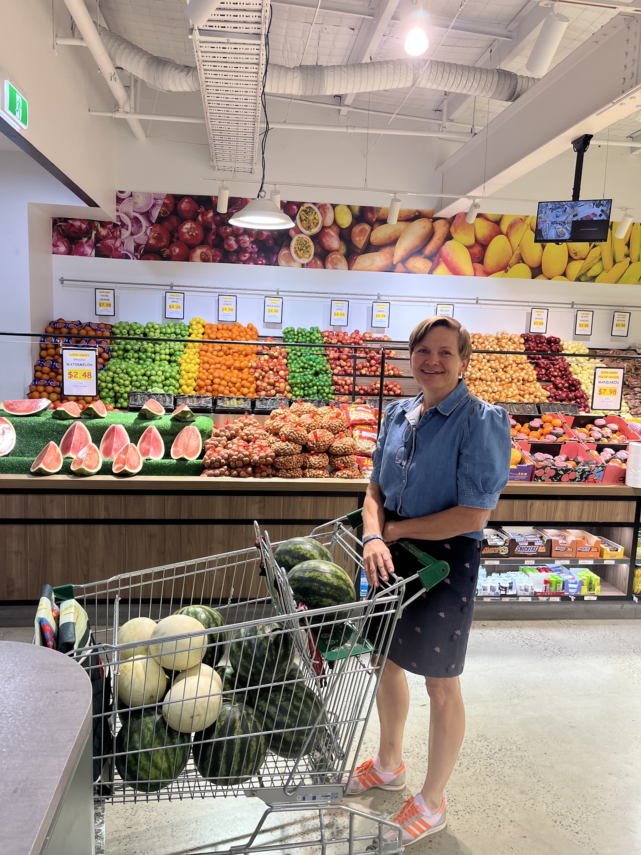A happy customer with a trolley of watermelons in front of the fruit wall